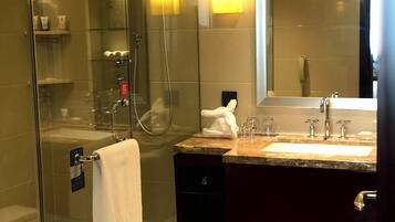 A modern bathroom with a glass-enclosed shower, a vanity with a sink and mirror, and toiletries on the counter.