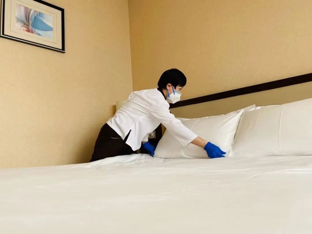 Una persona arreglando una cama en una habitación de hotel.