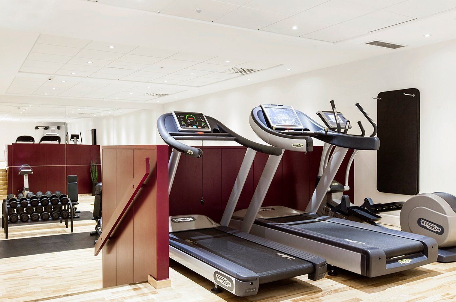 Un gimnasio con cintas de correr, un soporte para pesas y equipo de ejercicio.