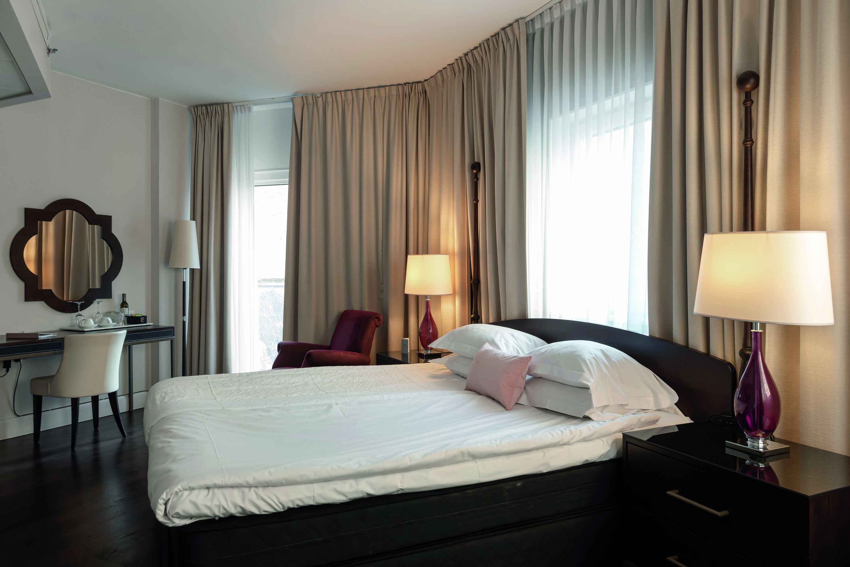 Habitación de hotel con una cama grande, un escritorio con silla, dos lámparas y un espejo en la pared.