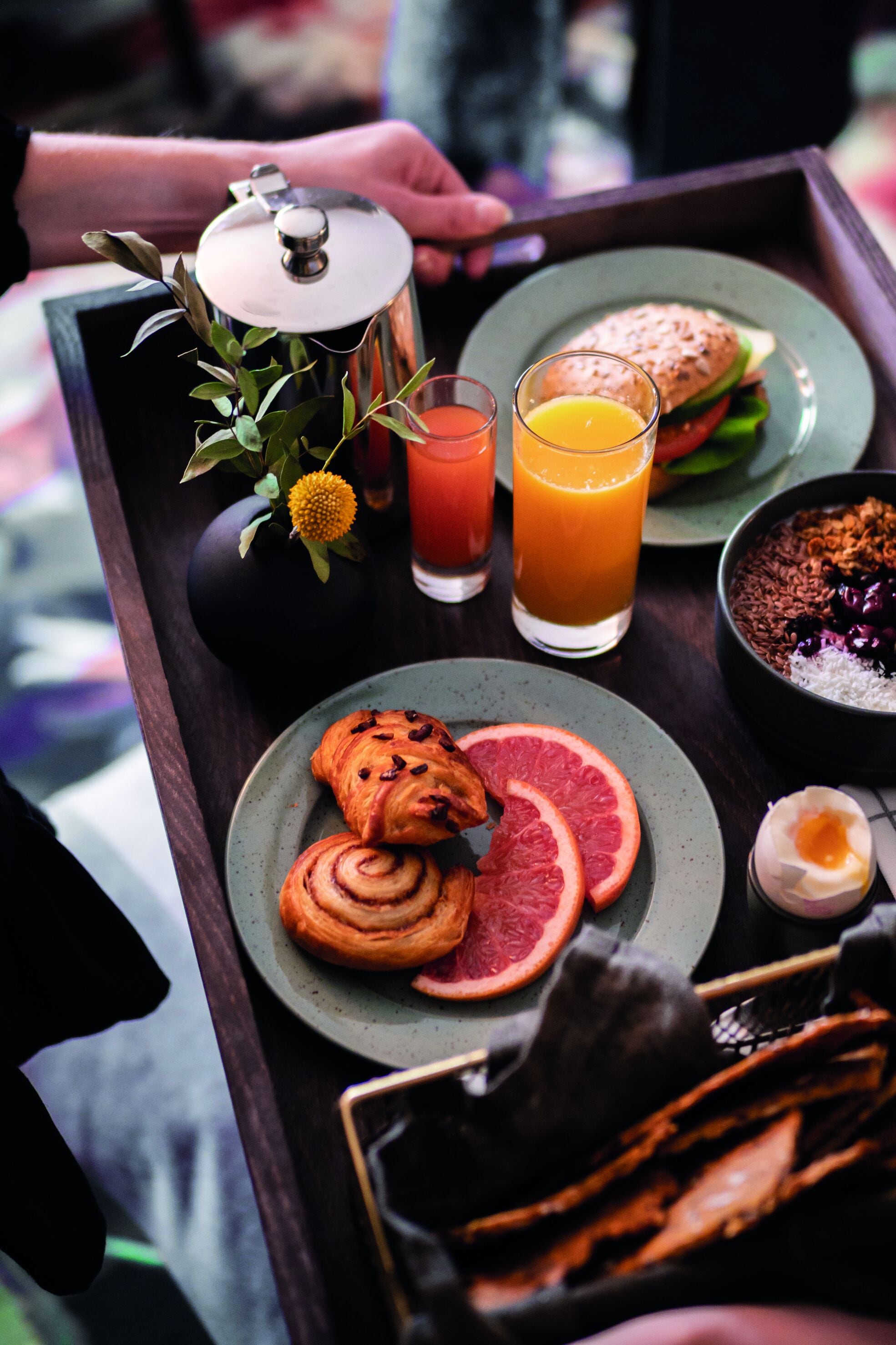 A tray with breakfast items including croissants, grapefruit slices, a sandwich, and a bowl of cereal.