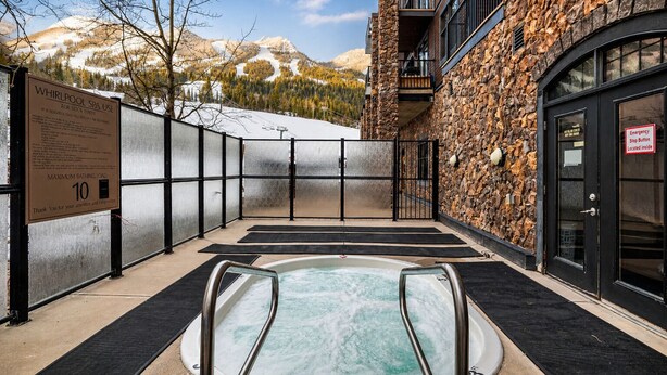 Un área de spa con un jacuzzi, un letrero que indica una capacidad máxima de 10 personas y vistas de montañas al fondo.