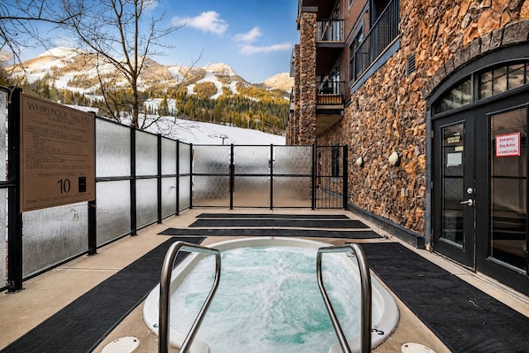 A spa area with a hot tub, a sign indicating a maximum bathing load of 10, and a view of mountains in the background.