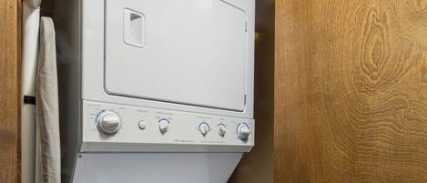 A compact laundry area with a front-loading washer and dryer, a wooden door, and a ceiling vent.