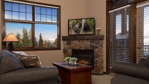 Una sala de estar acogedora con una chimenea de piedra, dos sofás grises, una mesa de centro con plantas y un televisor montado sobre la chimenea.