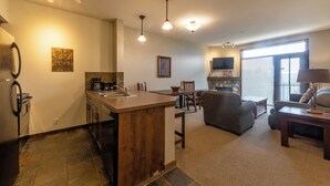 Una cocina moderna con una isla central, un comedor con sofá y sillas, y una sala de estar con televisor y chimenea.