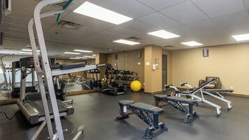 Un gimnasio con cintas de correr, elípticas, una prensa de banca y una pelota de ejercicios amarilla.