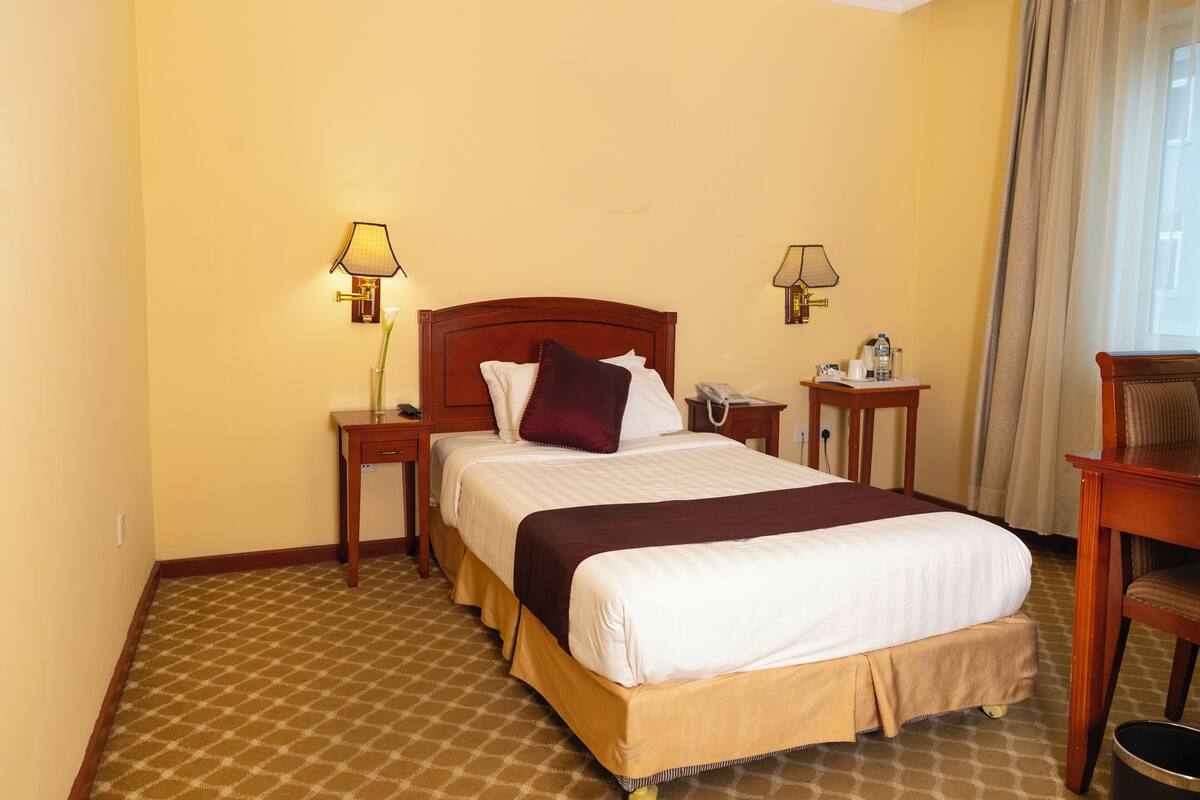 A hotel room with a large bed, two bedside tables, a chair, a lamp, and a window with curtains.
