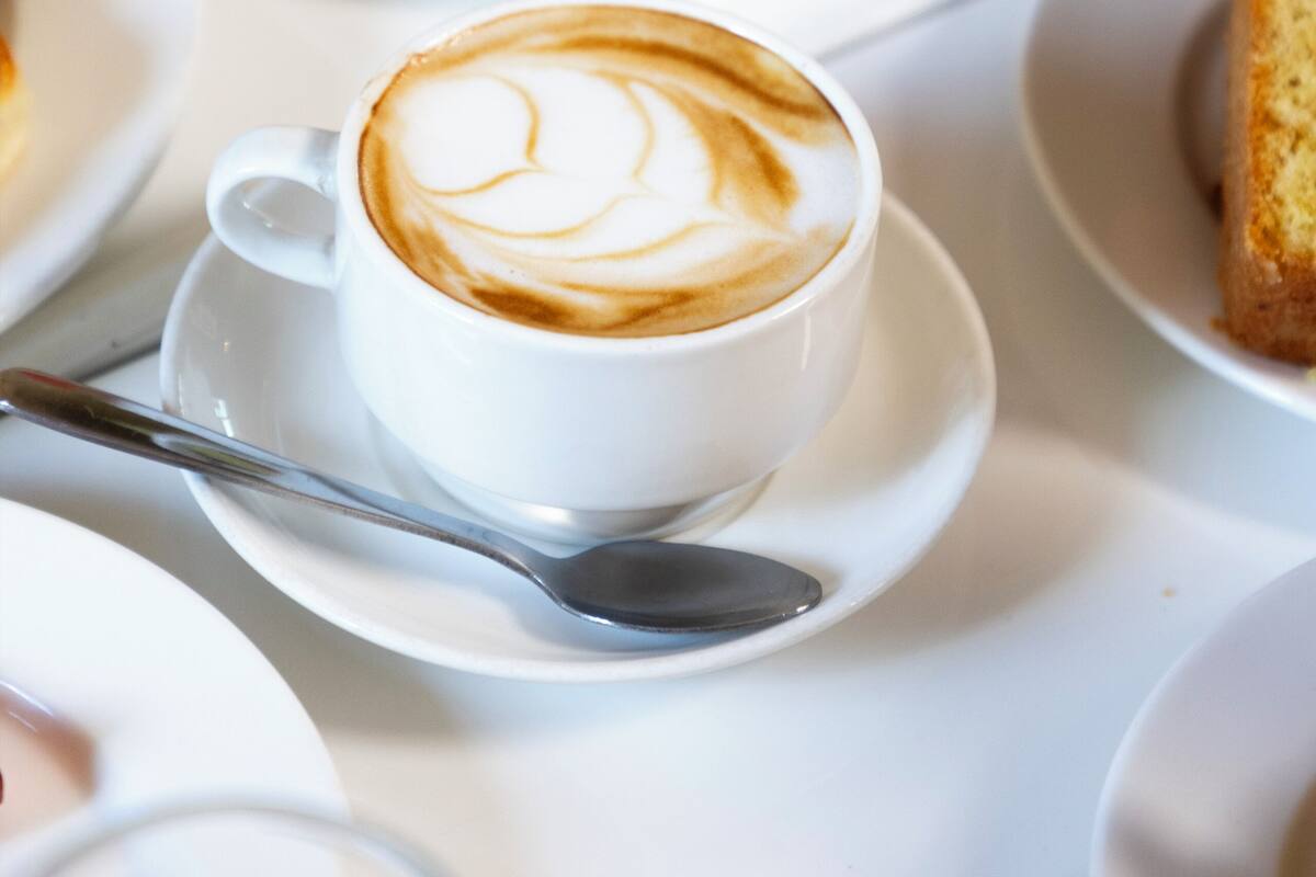 A table with a cup of coffee, a spoon, and a plate of food.