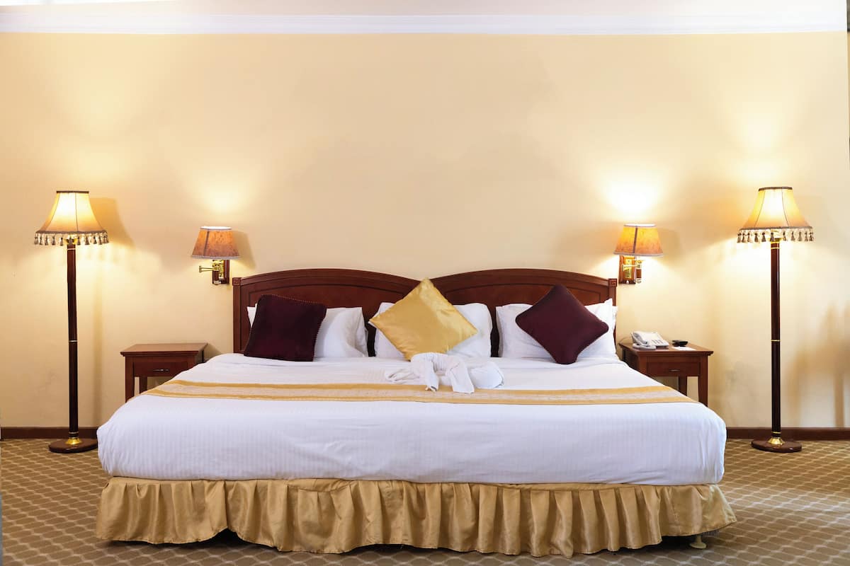 A neatly made bed with a gold skirt, two bedside lamps, and a telephone on the nightstand.