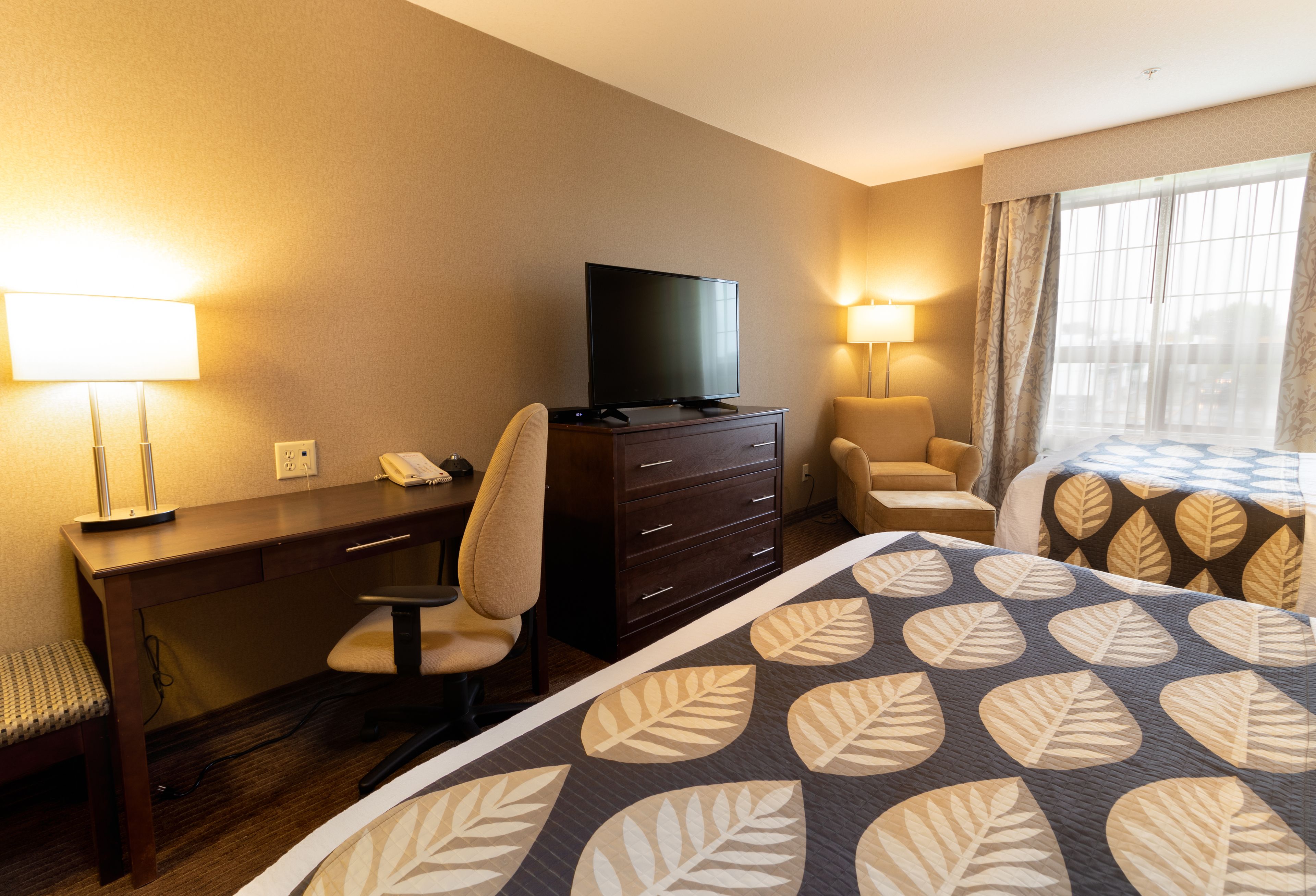 A hotel room with a bed, desk, chair, TV, and two lamps.