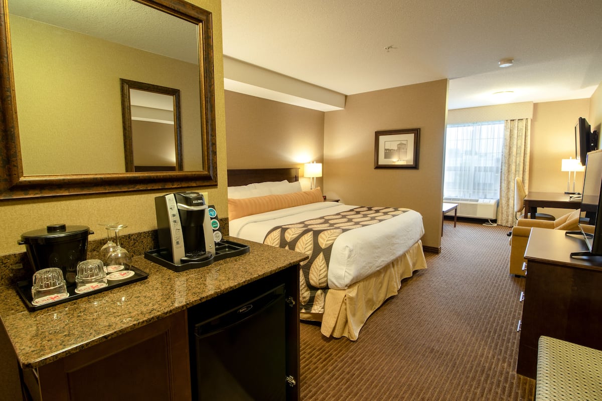 A hotel room with a bed, a desk, a coffee maker, and a mirror.