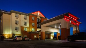 A hotel with a red and white sign, a parking lot, and a few cars.