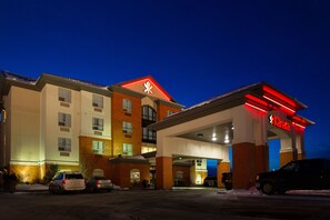 A hotel with a red and white sign, a parking lot, and a few cars.