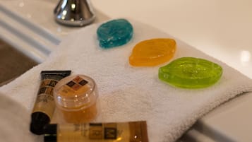Una toalla blanca con varios artículos de aseo, incluyendo un jabón azul, naranja y verde, una botella de loción y un tubo de crema.