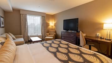 A hotel room with a large bed, a desk with a computer, a TV, a sofa, and a chair.