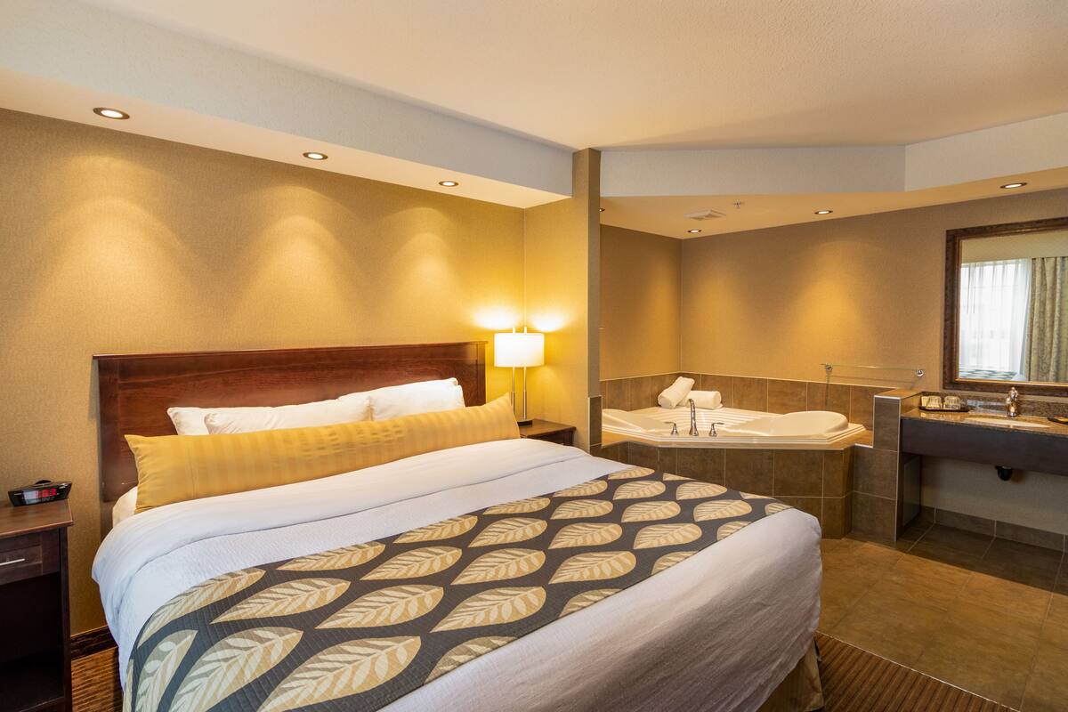 A hotel room with a large bed, a bathroom with a bathtub, and a vanity with a mirror.