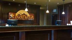 A reception desk with a wooden panel design, a sign reading "The Kanata By BCMinns", and two Samsung monitors. - The Kanata Inn Fort Saskatchewan (Fort Saskatchewan)