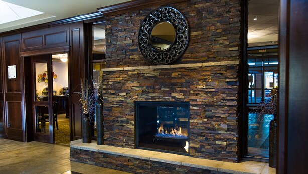 A stone fireplace with a fire, a mirror above it, and a wooden door to the left. - The Kanata Inn Fort Saskatchewan (Fort Saskatchewan)