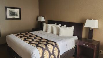 A hotel room with a large bed, two bedside tables, a framed picture on the wall, and a patterned throw blanket.