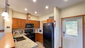 A modern kitchen with granite countertops, wooden cabinets, a black refrigerator, and a built-in oven. - Whispering Pines (Golden)