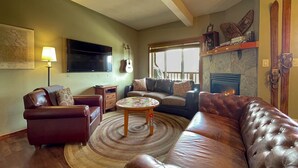 A living room with a leather sofa, a coffee table, a fireplace, a mounted TV, and a guitar. - Whispering Pines (Golden)