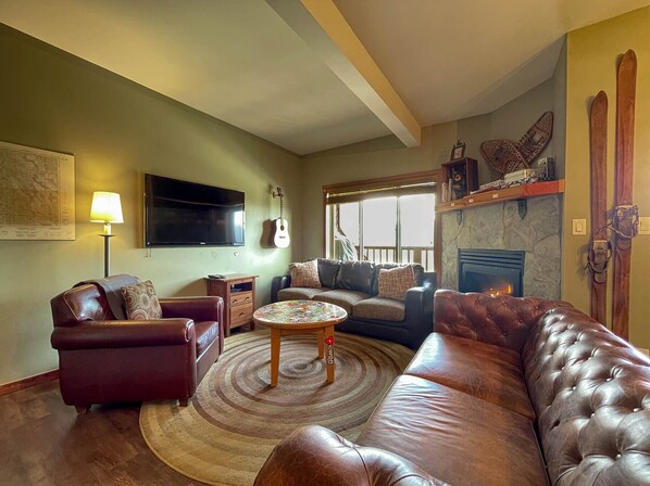 A living room with a leather sofa, a coffee table, a fireplace, a mounted TV, and a guitar.