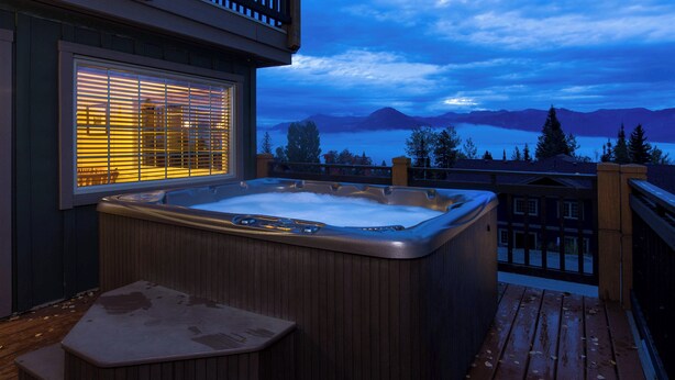 A hot tub on a wooden deck with a view of mountains and a lake. - Whispering Pines (Golden)