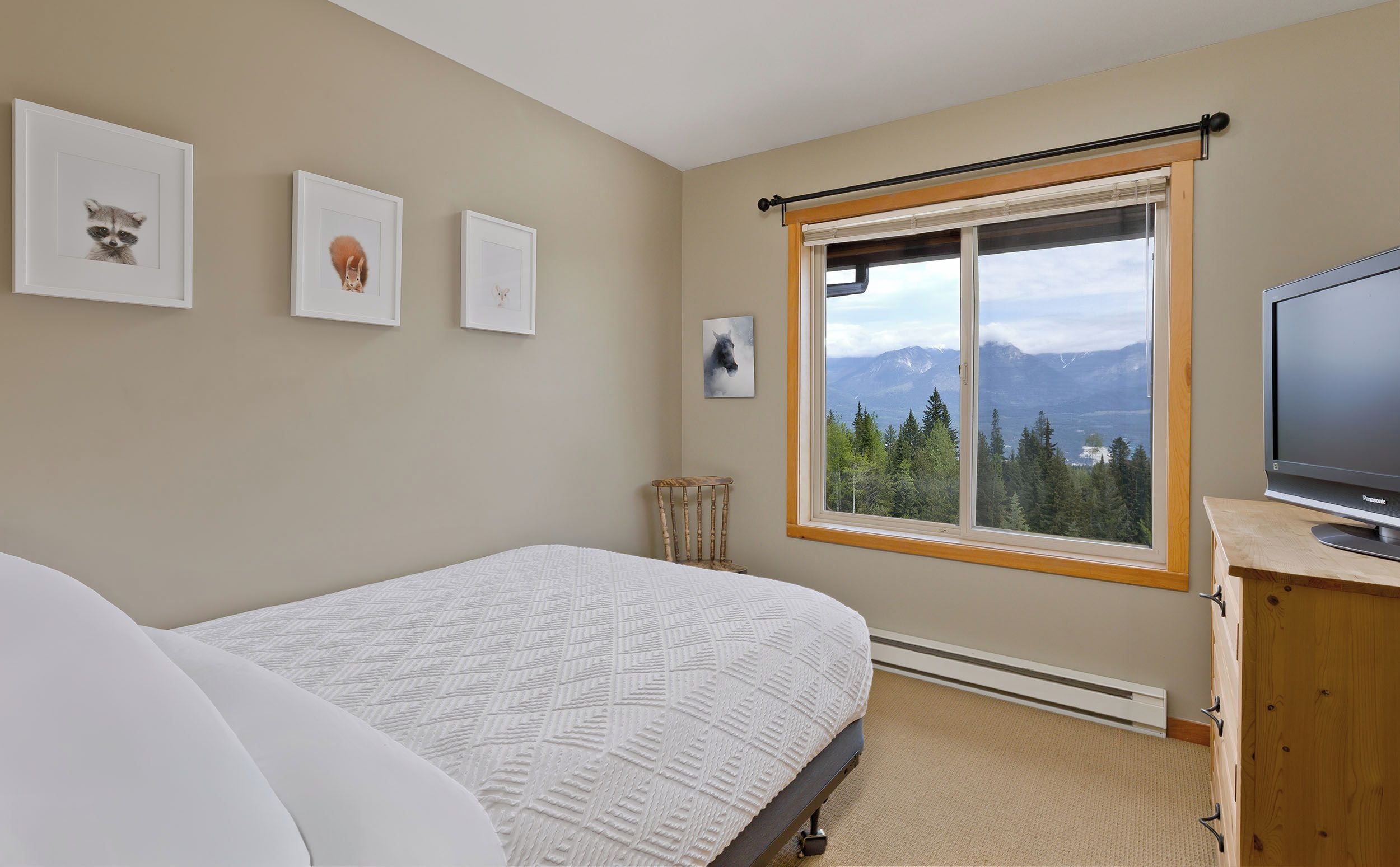 A bedroom with a bed, a television on a wooden cabinet, and a window with a mountain view.