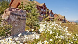 A lodge with multiple wooden cabins, a large rock with a name plaque, and a field of daisies. - Whispering Pines (Golden)