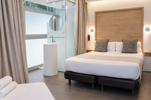 A modern hotel room with a large bed, a bedside table, a round mirror, a round light, and a view of greenery outside. - Casa Lit Barcelona (Barcelona)