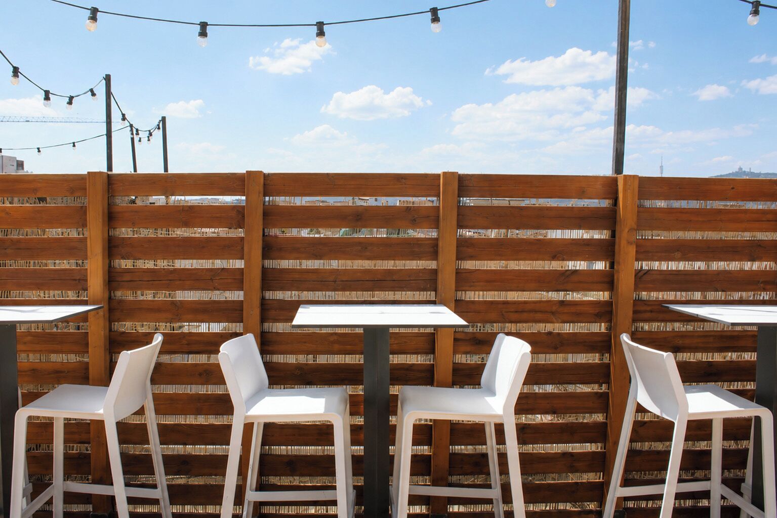 An outdoor seating area with tables and chairs, a wooden fence, and string lights.