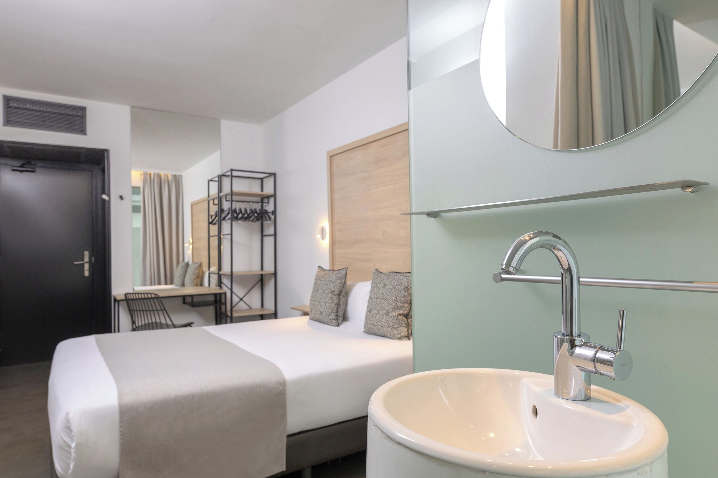 Een hotelkamer met een bed, nachtkastje, spiegel en wastafel.