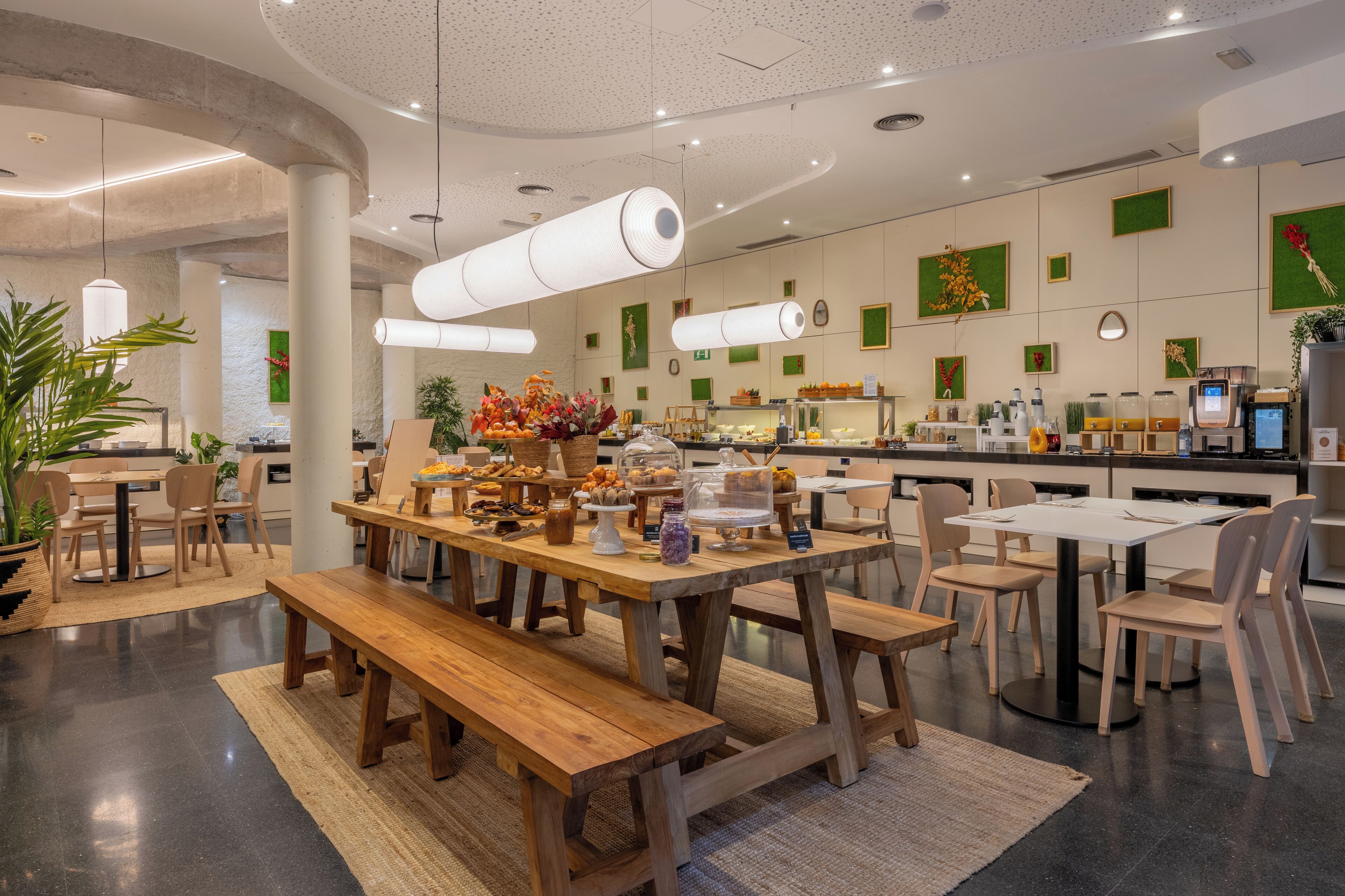 Un restaurante moderno con mesas y bancos de madera, diversas vitrinas con comida y una decoración interior limpia y contemporánea.