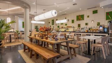 Un restaurante moderno con mesas y bancos de madera, diversas vitrinas con comida y una decoración interior limpia y contemporánea.