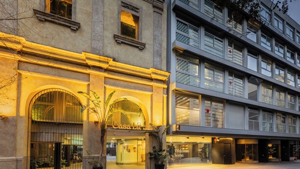 Una entrada de hotel con fachada clásica, un edificio moderno contiguo y un letrero acogedor.