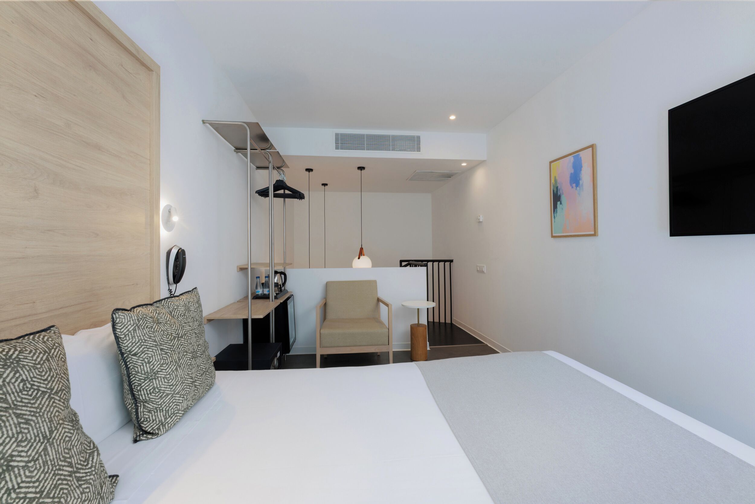 A modern hotel room with a bed, a desk, a chair, and a TV on the wall.