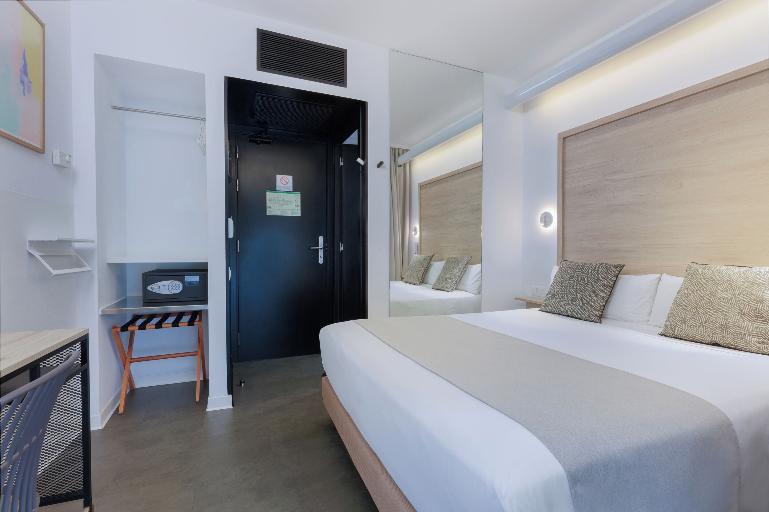 A hotel room with a bed, a desk, and a door.