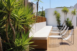 An outdoor seating area with a long bench and round tables, surrounded by potted plants and palm trees. - Casa Lit Barcelona (Barcelona)