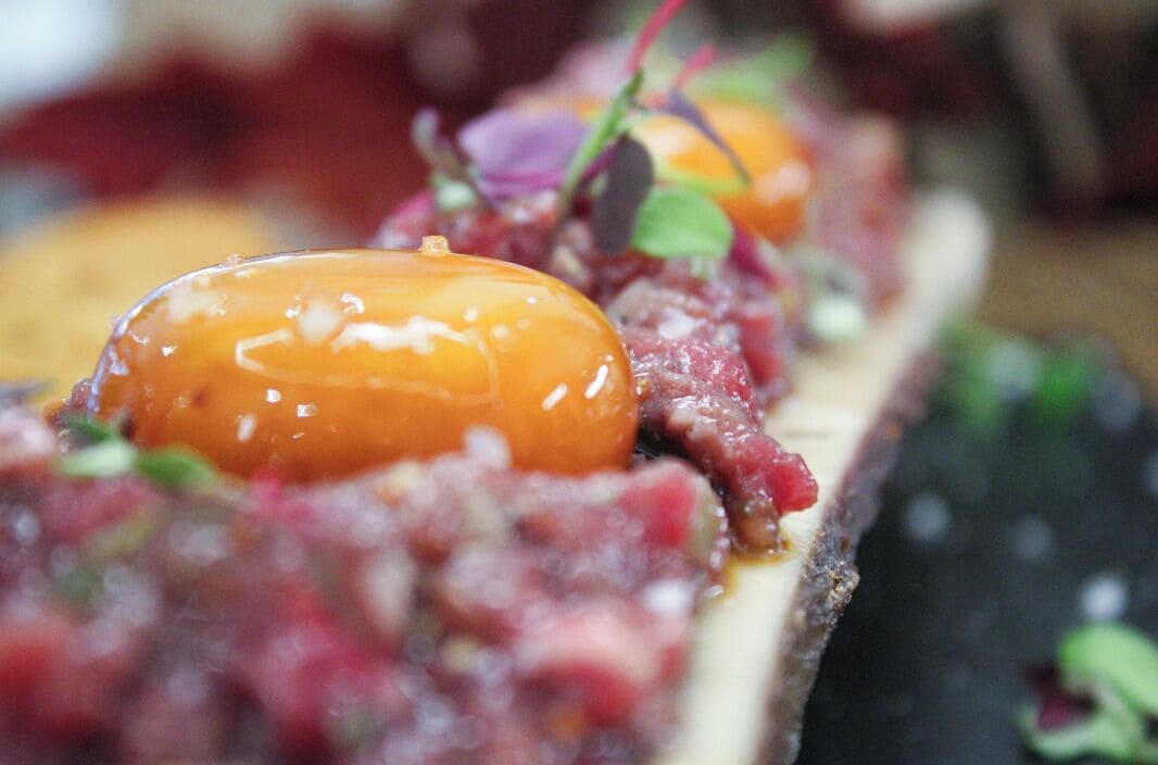 Primer plano de un plato con un huevo escalfado, adornado con microgreens y quizás algunas hierbas, servido sobre una rebanada de pan o galleta.