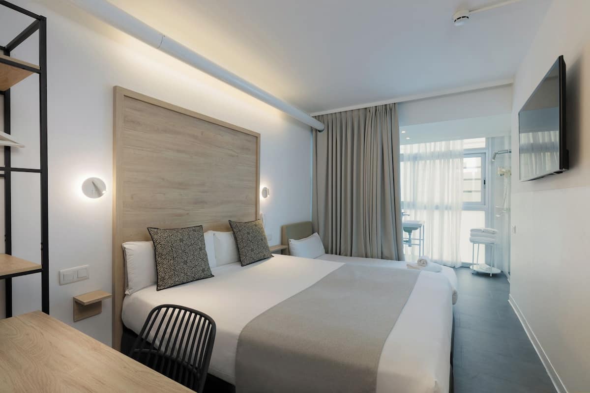 A modern hotel room with a large bed, bedside tables, a desk, and a TV mounted on the wall.