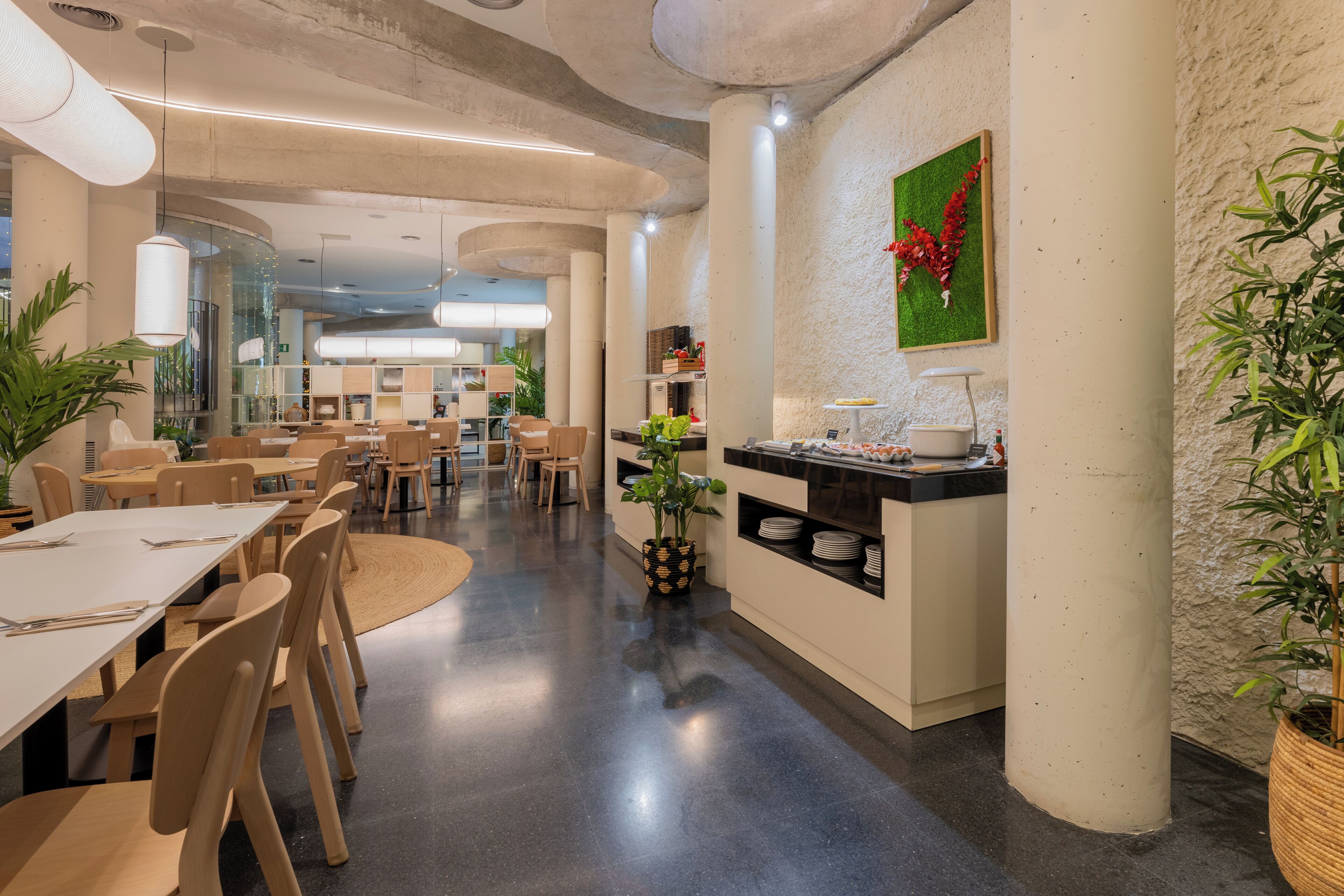 A modern dining area with high tables and chairs, a buffet counter, and decorative plants.