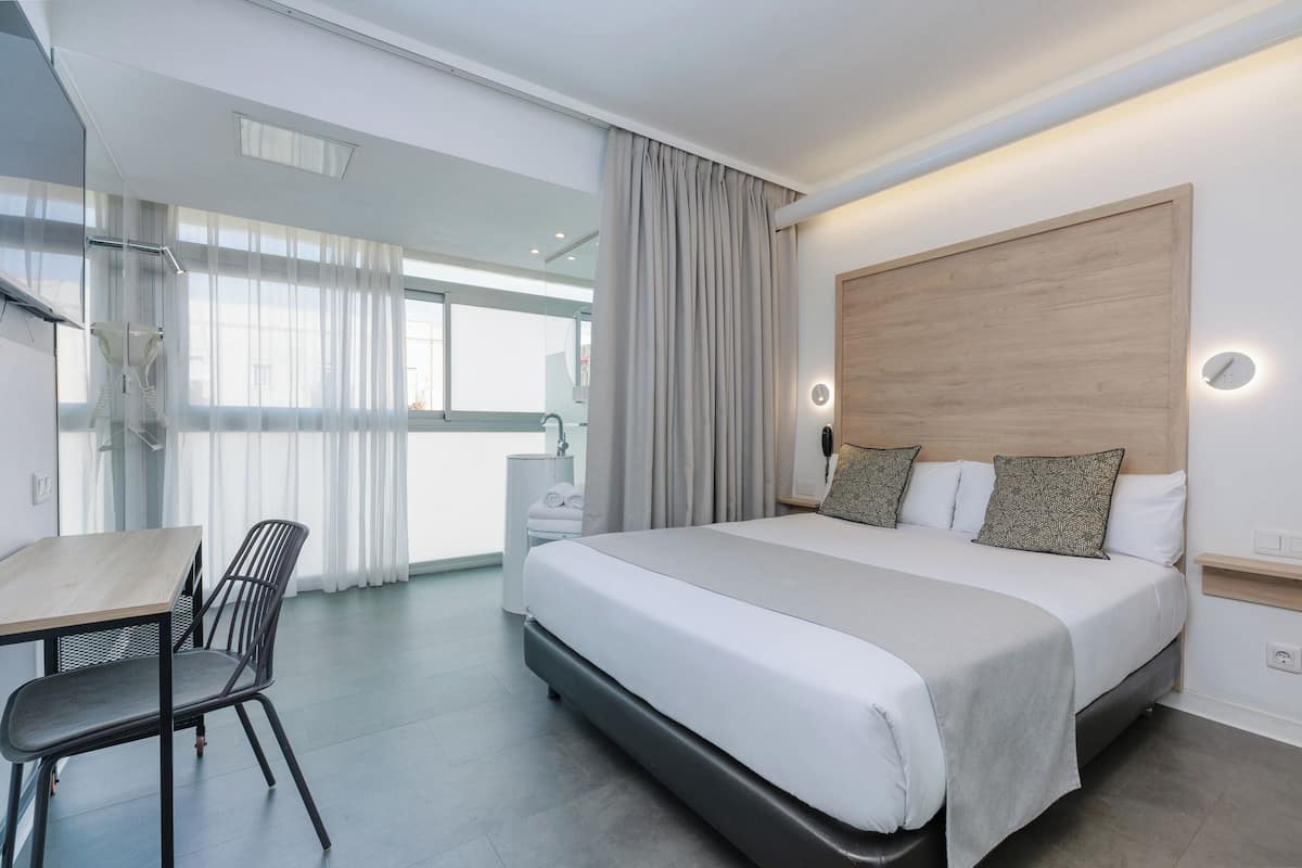 A modern hotel room with a large bed, a desk, and a chair.