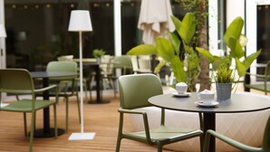 Un café con mesas redondas, sillas verdes y una planta en maceta sobre una de ellas.