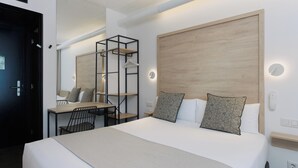 Una habitación de hotel moderna con una cama grande, un escritorio con silla, un espejo y cabecera de madera.