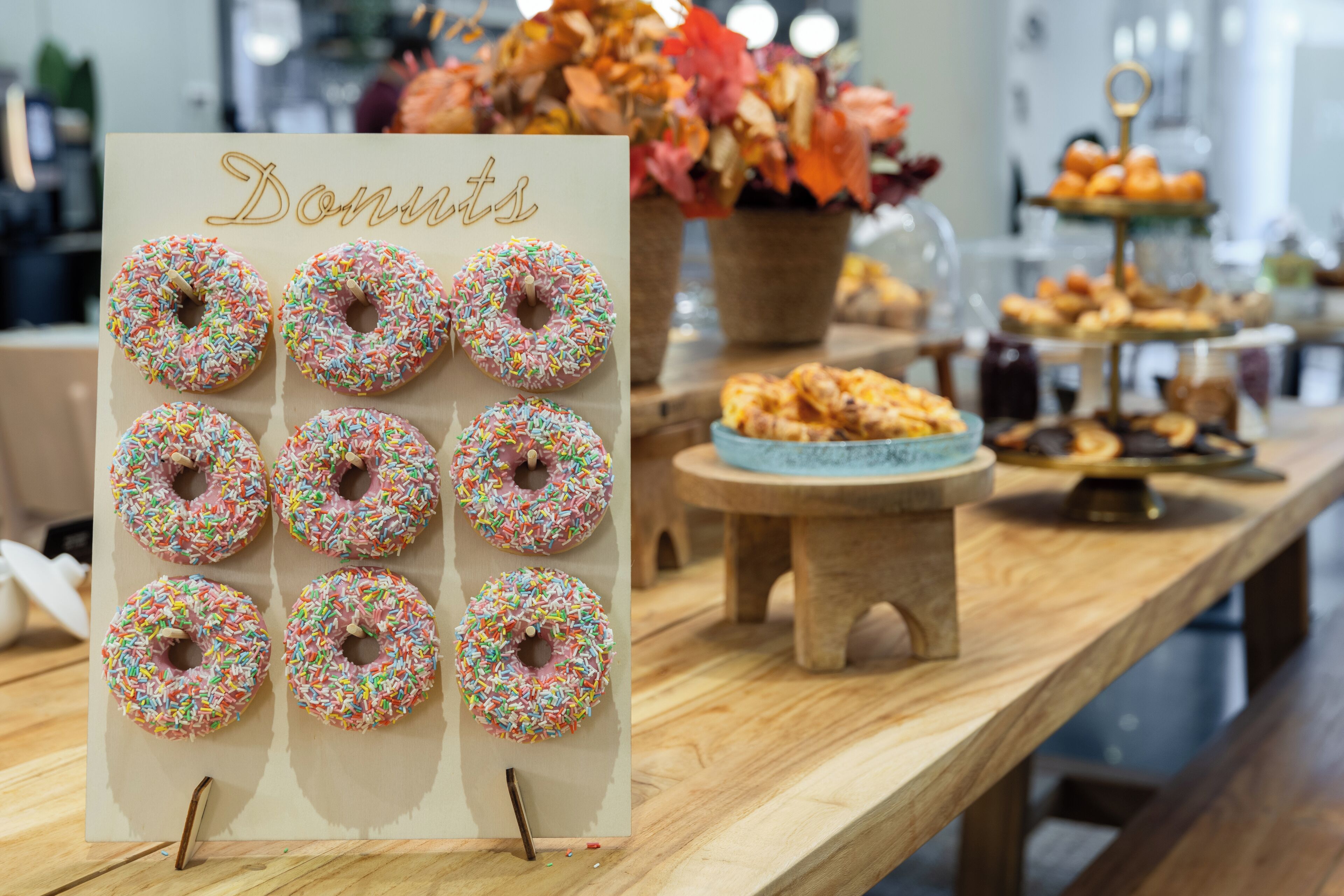 A display of donuts with a sign reading "Donuts" and a variety of pastries on a wooden table.