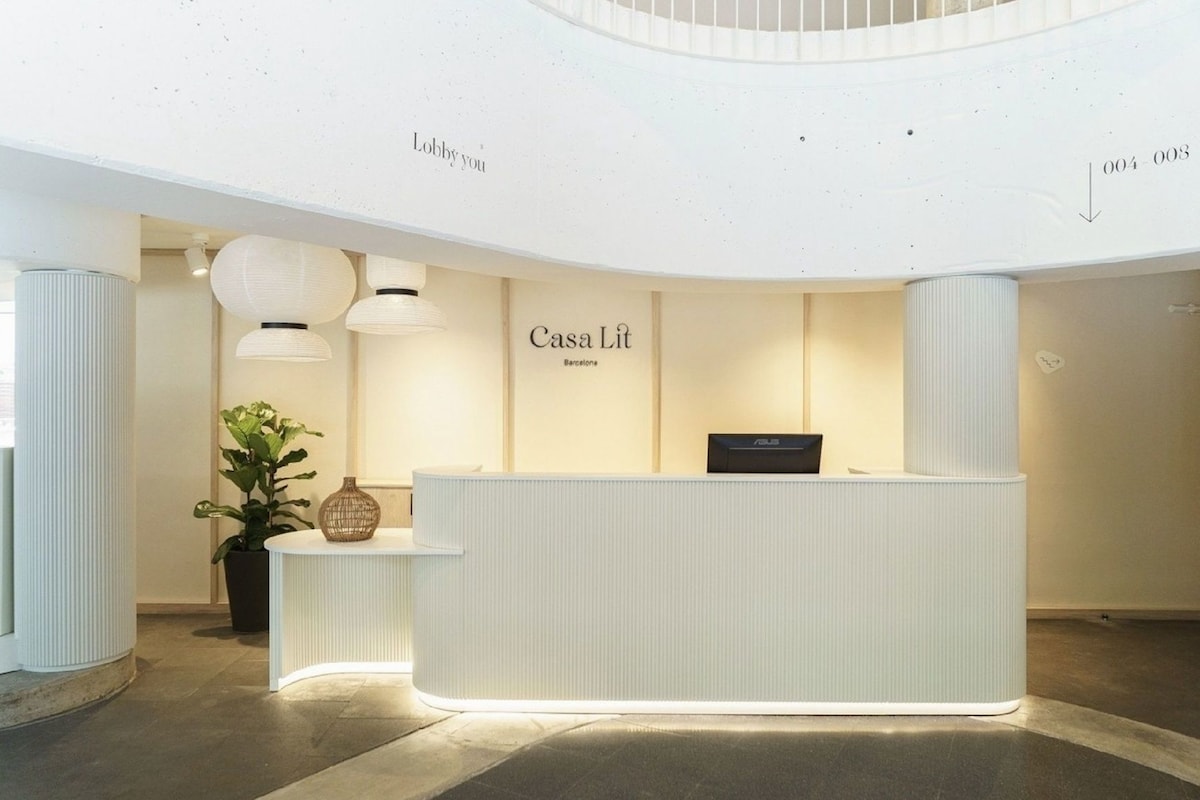 En receptionsdisk med en skylt som visar texten ”Casa Lit Barcelona” i en modern lobby med ett välvt tak och en krukväxt.