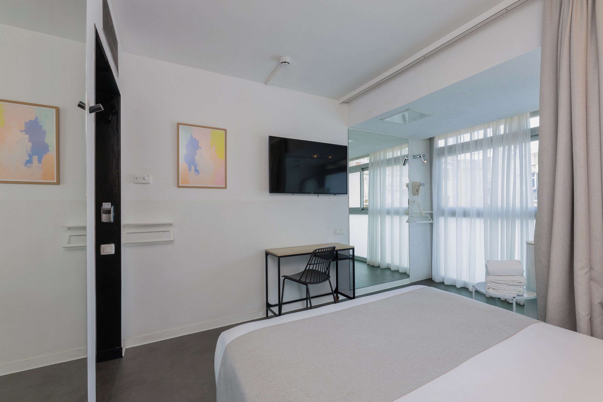Habitación de hotel moderna con una cama grande, un escritorio con silla, un televisor montado en la pared y un espejo grande que refleja la habitación.