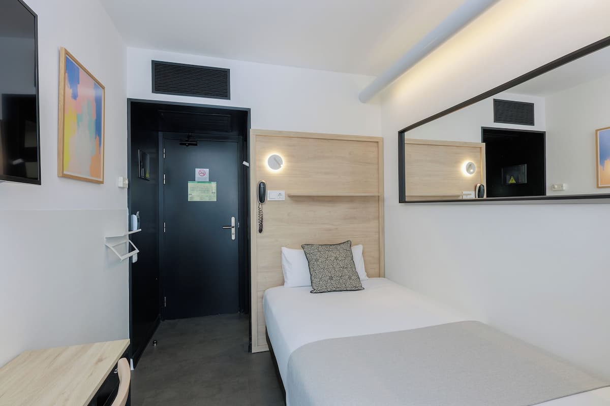 A hotel room with a bed, a desk, a mirror, and a door.
