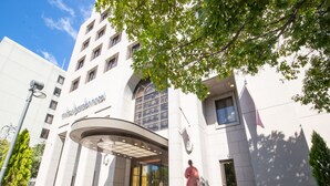 A hotel entrance with a curved canopy, large windows, and a person carrying luggage. - Mitsui Garden Hotel Hiroshima (Hiroshima)
